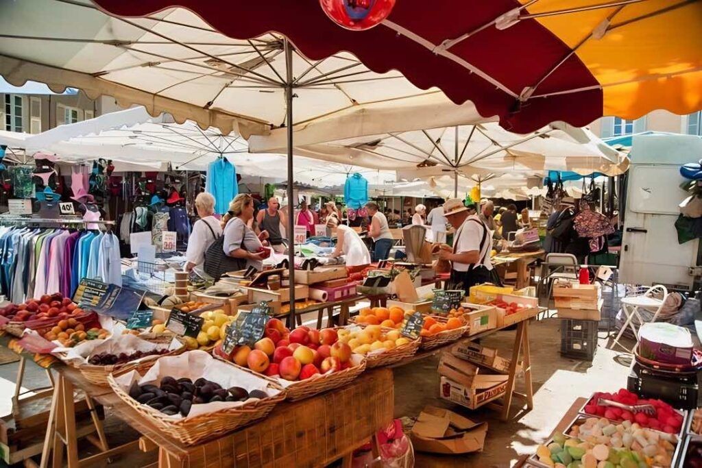 Busy outdoor market with people browsing fruit and clothing stalls under large shaded canopies.